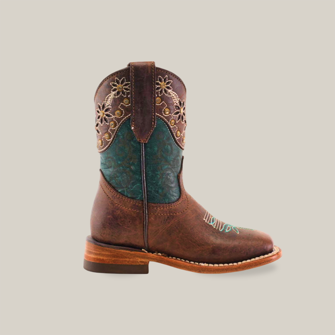 The Grecas Tabaco - Square Toe is a single brown cowboy boot featuring a decorative teal shaft with intricate floral embroidery. Made from premium leather, it has a low heel and rounded toe, showcasing detailed stitching on the vamp that reflects traditional craftsmanship.