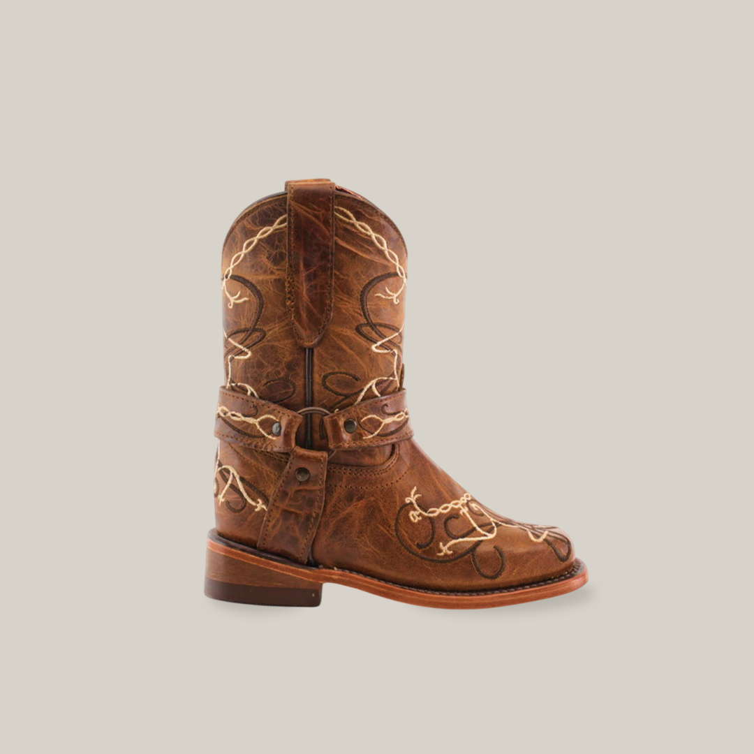 The Graffiti Yellow - Rodeo Toe is a small brown genuine leather cowboy boot featuring intricate white embroidery and decorative stitching, capturing the spirit of young cowgirls. It has a thick heel and a loop for easy wearing, set against a plain white background.