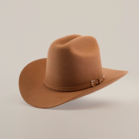 The 6X 2 Carnales Fawn is a brown felt cowboy hat with a classic curved brim, top crease, and decorative band featuring a metal buckle, all set against a neutral background. This iconic piece embodies timeless western style and rugged elegance.