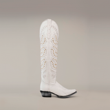 The Crystals Wings Frost White boot features intricate gold and silver cutout designs on a white knee-high shaft, with a leather sole, pointed snip toe, and low black heel, set against a simple gray gradient background.