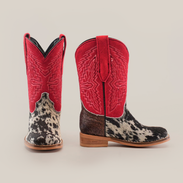 The Cowhide Hair Pinto Square Toe boots showcase red uppers with intricate stitching, complemented by black and white speckled cowhide lower sections. Their western style comes complete with brown soles, all set against a plain white background.