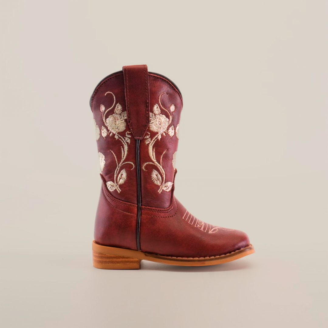 The Jatziry Cogñac Square Toe boot for little girls features intricate white floral embroidery on handcrafted leather, a pull strap, and a wooden heel—an ideal choice for budding cowgirls.