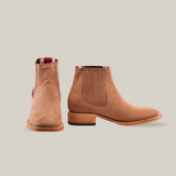 The Prime Suede Sand Square Toe boots, featuring a square toe and side elastic panels, have a flat heel and subtle decorative stitching in cowboy fashion, displayed on a white background. The brown leather design includes visible inside lining at the top edge.