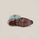 A single Premier Tabaco boot lies on its side, showcasing the ornate brown sole with detailed engravings. The turquoise upper boasts decorative stitching and patterns that reflect Western elegance, all set against a plain white background.