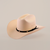 The 500X Sinaloa Straw Hat is a cream-hued cowboy hat with a slightly curved brim and indented crown, set against a plain white backdrop. It boasts timeless style and top-notch quality, featuring a black band with decorative emblems around the crowns base.