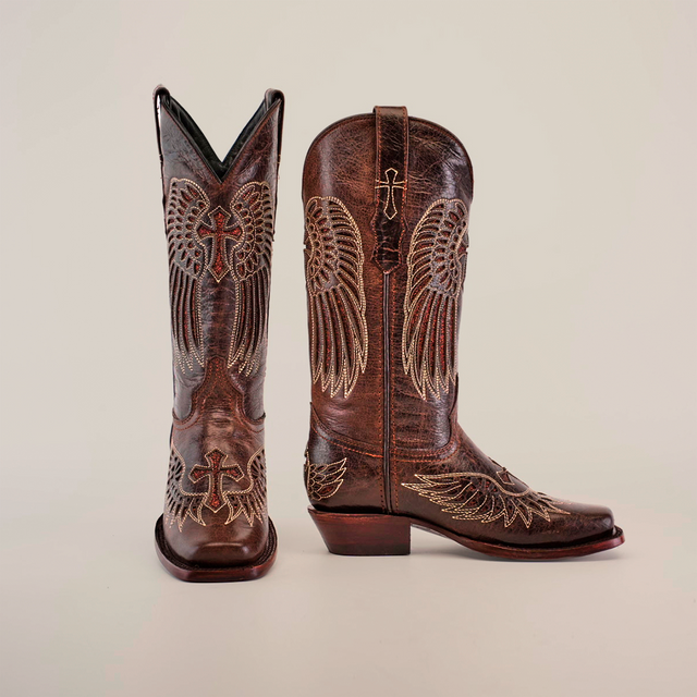 Introducing the Texas Cross Glitterbomb Brown boots: crafted from premium leather with intricate wing and cross embroidery. One boot stands upright, the other slightly angled against a white backdrop, showcasing expert craftsmanship.