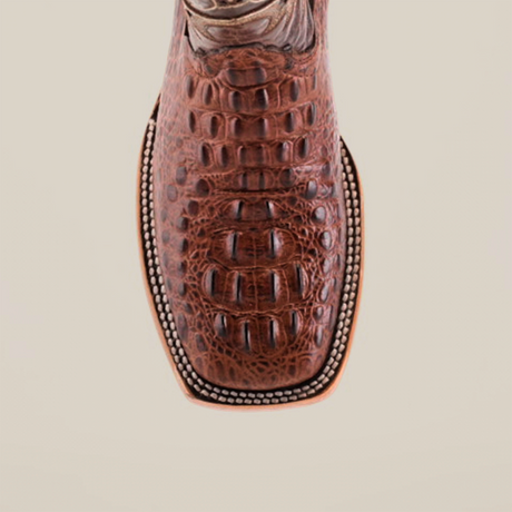 Close-up of the toe of a Caiman Hornback Print Chocolate Square Toe cowboy boot, highlighting its luxurious reptile-like pattern and intricate stitching detail on a light background.