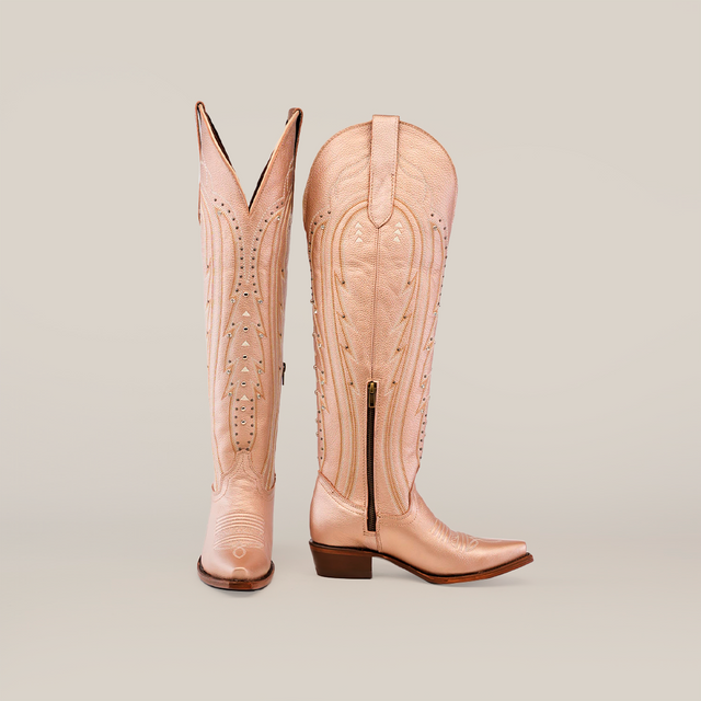 The Sara Metalic Florentine boots are tall beige cowboy boots with intricate stitching, featuring a snip toe, low heel, and visible side zipper. One boot is upright showing its front design while the other displays a side profile.