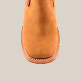 The Prime Suede Honey Square Toe is a tan suede ankle boot viewed from above, highlighting its stylish square toe and part of the upper. It features detailed stitching along the sole edge and boasts a smooth suede texture.