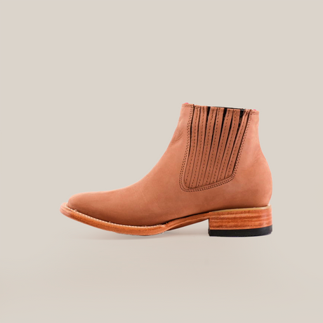 The Prime Suede Sand Square Toe is a tan leather ankle boot with side elastic panels for easy slip-on and a wooden stacked heel. Its sleek design, perfect for a fashion-forward wardrobe, is showcased on a plain white background to emphasize its elegance.