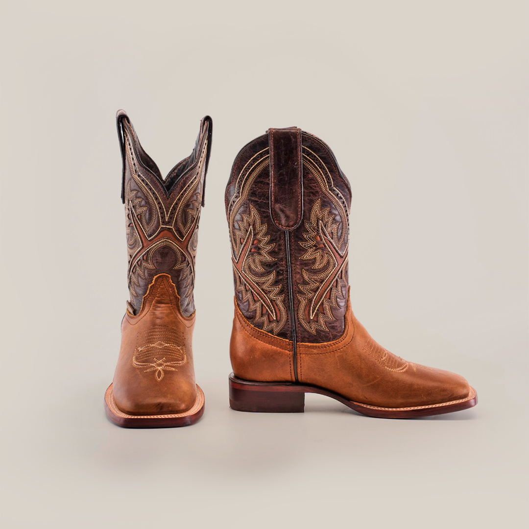 A pair of Cater Honey Square Toe boots, crafted from premium leather with detailed brown and tan stitching, is displayed on a white background. One boot stands while the other tilts, showcasing the superior craftsmanship and intricate embroidery around the shaft.