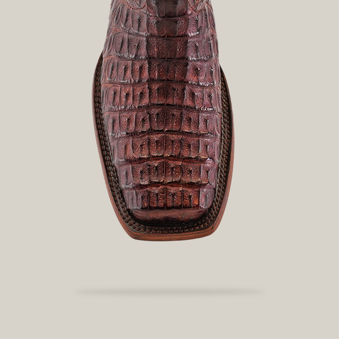 Close-up of a single Exotic Caiman Hornback boot in rich brown, showcasing luxurious hornback details with a Rodeo toe against a neutral background.