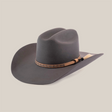 The 6X Doble SS Gris Oxford is a dark grey felt cowboy hat made from premium sheeps wool, featuring a wide brim and a decorative tan band with a small black tassel and light-colored horsehair tuft, elegantly angled against a white background.