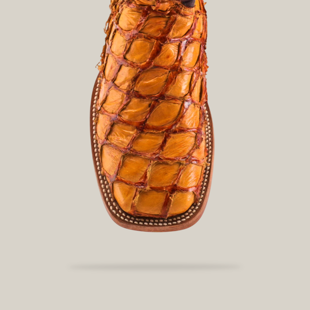 Close-up of the Exotic Piraruco Fish - Brandy cowboy boot, crafted from distinct pirarucu leather and featuring detailed stitching. The square toe, a signature of classic cowboy style, is highlighted against a plain beige background.