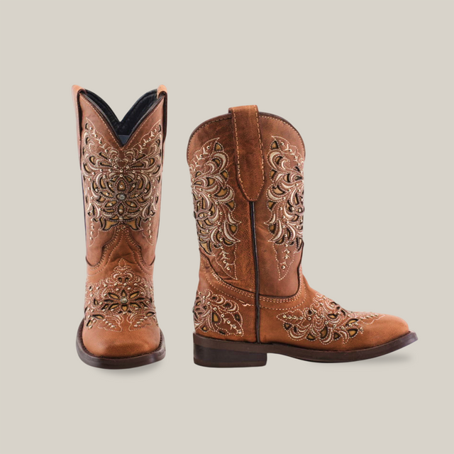 The Kiara Studs Fawn - Square Toe boots are crafted from premium leather in brown, adorned with ornate floral and swirl embroidery. Perfect for fashion-forward young girls, they stand upright on a white background, showcasing both side and front views effortlessly.