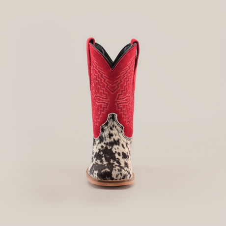 The Cowhide Hair Pinto Square Toe cowboy boot features a vibrant red shaft with detailed embroidery. Its foot showcases a unique black-and-white speckled cowhide design, resting on a light brown sole, embodying true western style, all displayed on a white background.