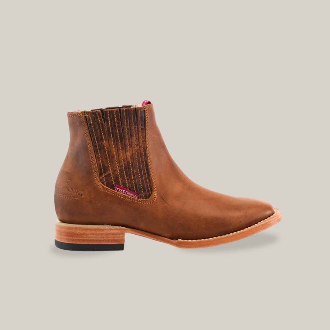 The Avejentado Honey square Toe is a brown leather ankle boot with subtle stitching, featuring a low wooden heel and side elastic panels. Its squared-off pointed toe and avejentado honey finish make it perfect for the cowboy scene.