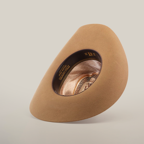 The 6X Country Fawn cowboy hat is shown upside down, revealing its intricate interior details. The brown felt hat boasts a patterned inner band with Resistol printed inside, all elegantly contrasted against a plain white background.