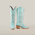 The Amara BB Suade boots feature a tall turquoise shaft with intricate white stitching, an elegant snip toe, and a stacked wooden heel, beautifully showcased against a plain white background.