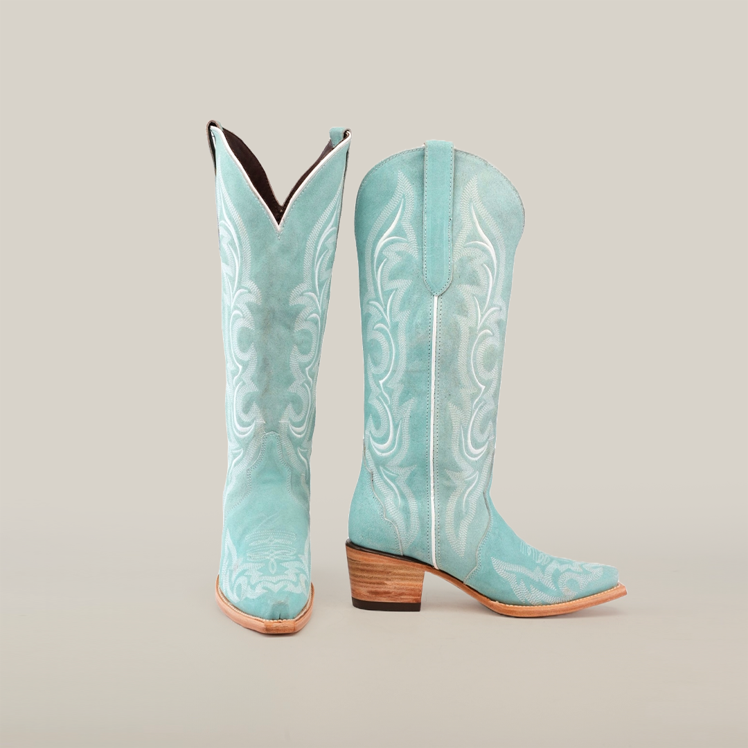 The Amara BB Suade boots feature a tall turquoise shaft with intricate white stitching, an elegant snip toe, and a stacked wooden heel, beautifully showcased against a plain white background.