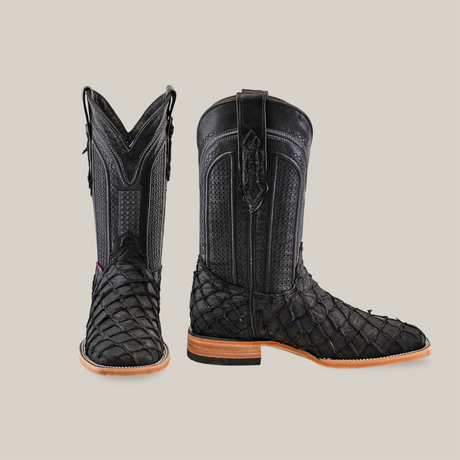 A pair of Exotic Piraruco Fish Matte Black square toe cowboy boots with textured reptile pattern and wooden soles stand upright on a white background, showcasing their authentic leather, detailed stitching, and pull straps.