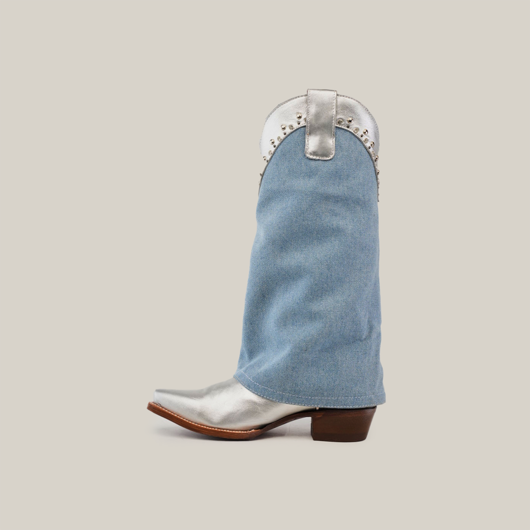 Introducing the Bella Denim Silver - Tall Shaft - Snip Toe, a standout womens cowboy boot featuring a denim fabric shaft with silver accents and metal studs, complemented by a light gray backdrop and convenient side pull tab.