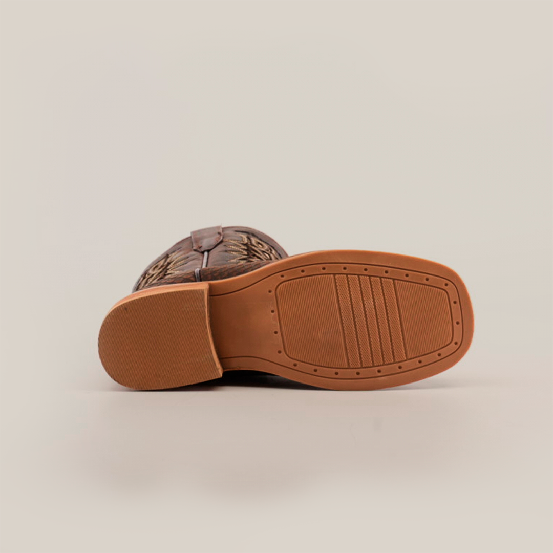 The image features the light brown cowhide leather sole of a Python Print Matte Brown Square Toe cowboy boot, showcasing a textured grip with a rectangular pattern. The darker brown upper is partially visible.