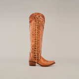 The handcrafted Tania Fawn boot features a tall shaft, snip toe, and ornate stitching. Its a single brown leather cowboy boot with a prominent lace-up design and low heel on a luxurious leather sole against a plain white background.