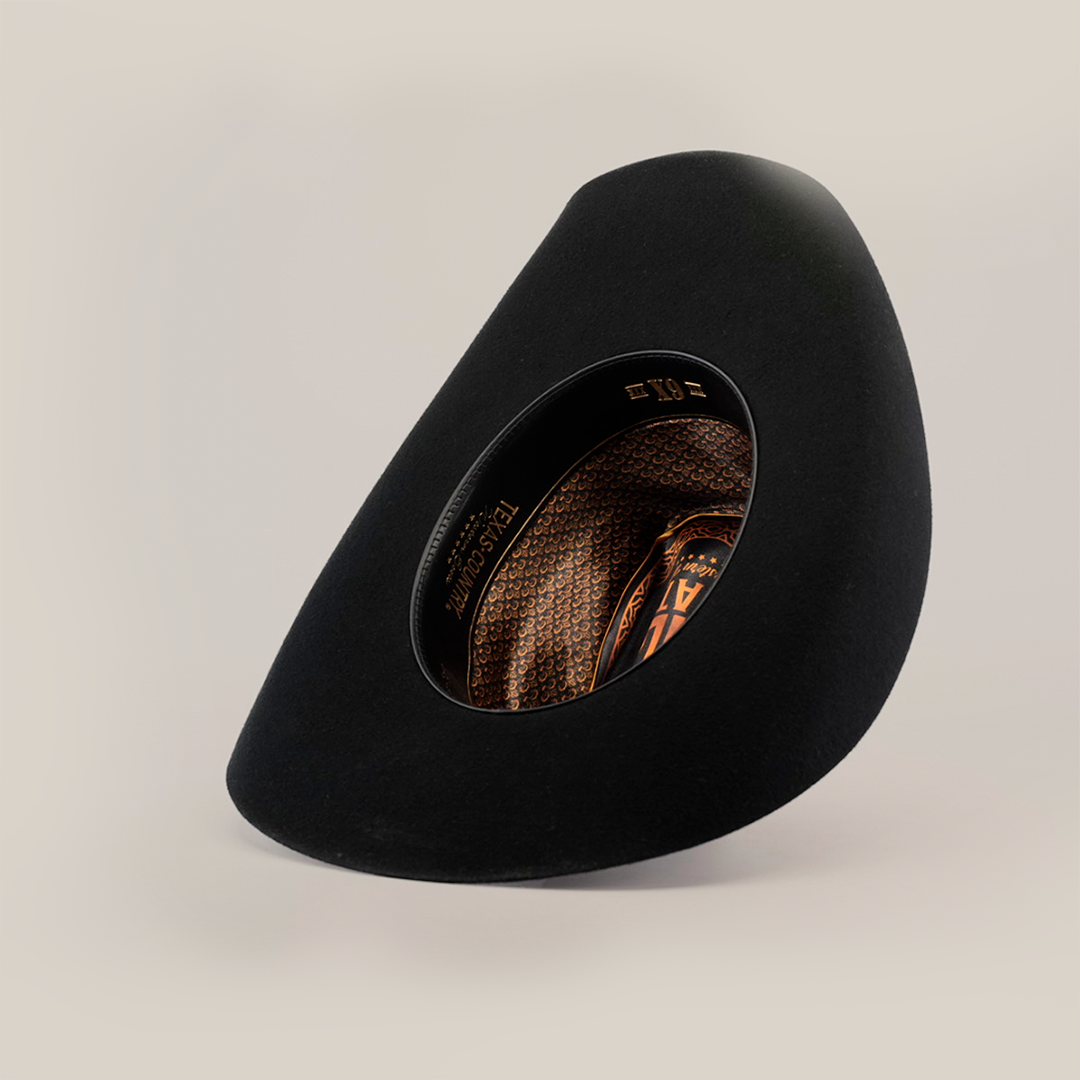 The 6X Bull Black hat, featuring an asymmetrical wide brim and a patterned brown interior, is set upright on a white background. Its unique shape exudes an artistic, modern vibe and captures the luxury essence of western wear.