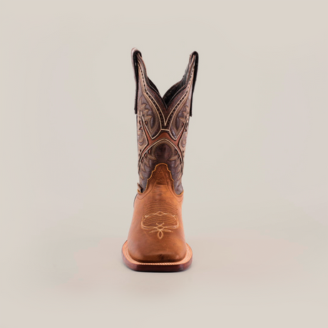 The Cater Honey Square Toe cowboy boot, made from premium brown leather, stands upright on a plain white background. It features intricate stitching and patterns, showcasing superior craftsmanship with a pointed toe and tall shaft adorned with decorative designs.