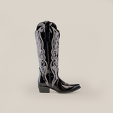 The Artemisa Patent Black - Tall Shaft - Snip Toe boot features intricate silver embroidery on premium leather, with a snip toe and low heel. Ornate stitching elegantly decorates the shaft against a plain white background.