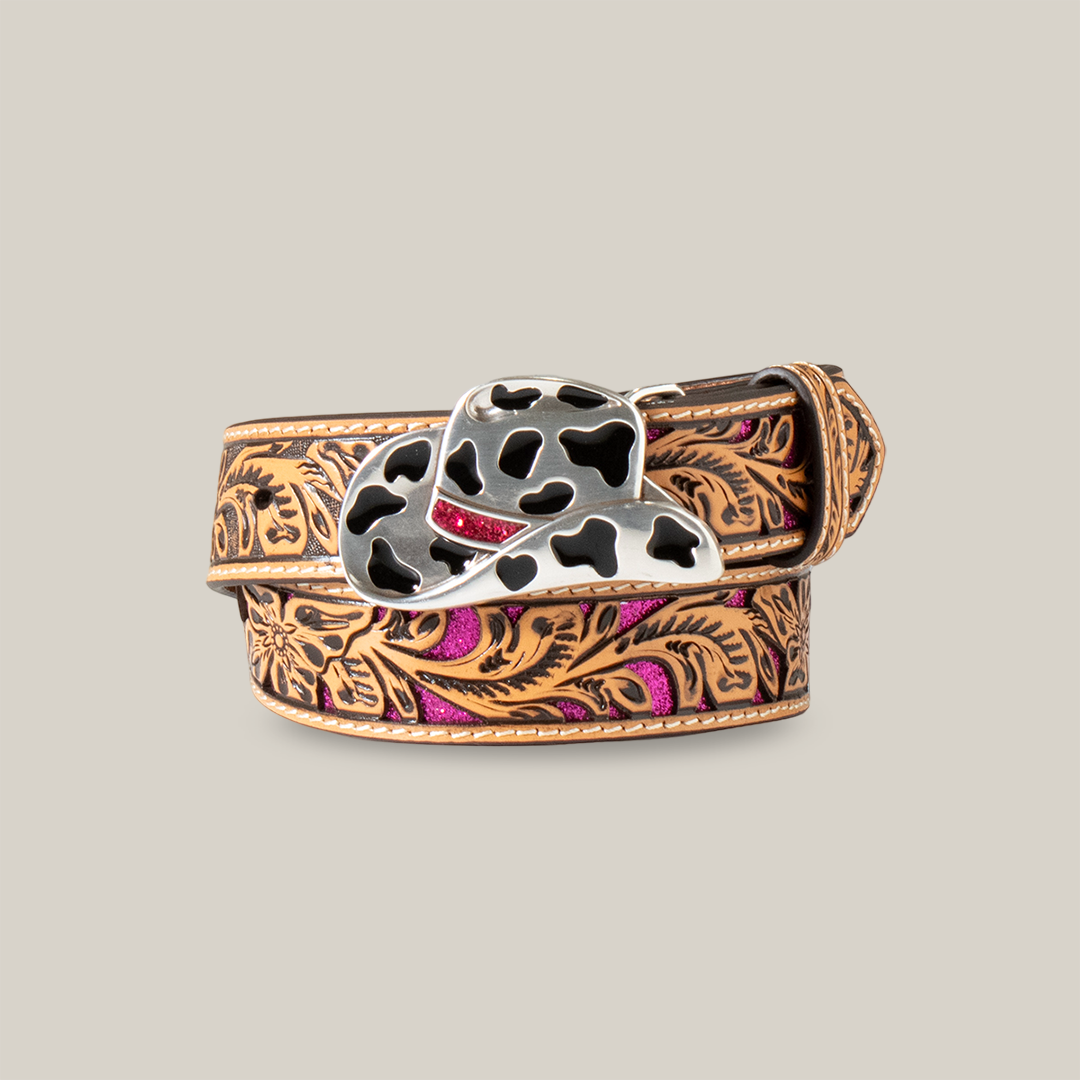 The Angel Ranch Western Girl Belt, model D130003648, is a coiled cowboy-style belt with intricate brown floral engravings and pink accents. It features a metal buckle shaped like a cowboy hat with black cow print patterns, set against a light beige background for Western-inspired flair.