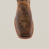 The Azkar Tan Square Toe cowboy boot features handcrafted cowhide leather with intricate white stitching on the toe and a decorative pattern. It has a rugged texture with a light brown sole, highlighted by visible white stitching around the edge for a refined look.