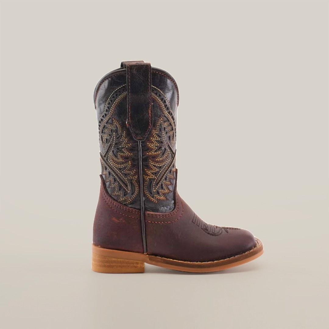 The Salvage Almond Square Toe boot for children features intricate embroidery on the shaft, crafted from premium cowhide leather. It has a low wooden heel and a rounded toe, elegantly showcased against a plain white background.