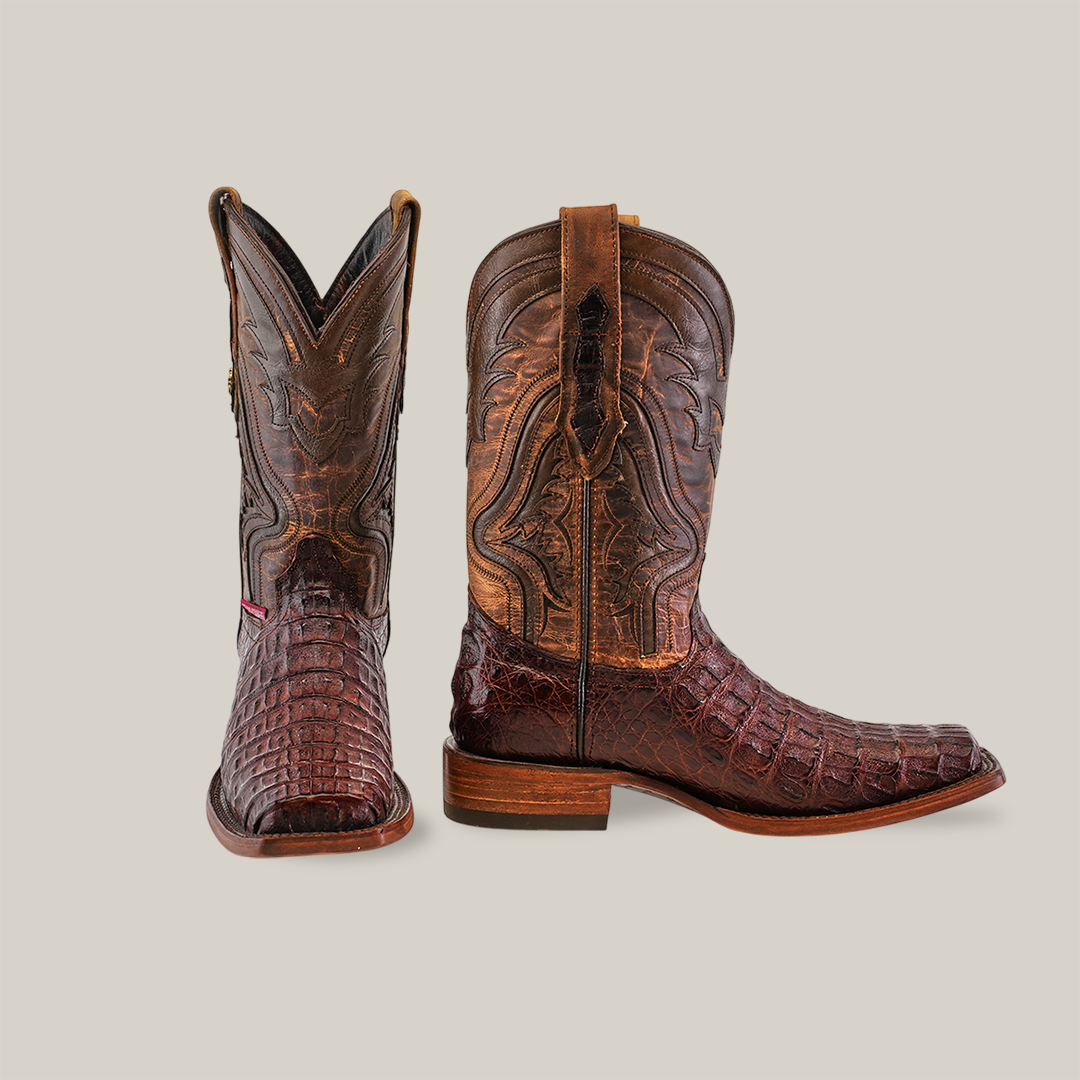 A pair of Exotic Caiman Hornback cowboy boots in brown with intricate stitching is displayed on a white background. The left boot shows the rodeo toe, while the right boot reveals a side view, emphasizing the detailed leather texture and design.