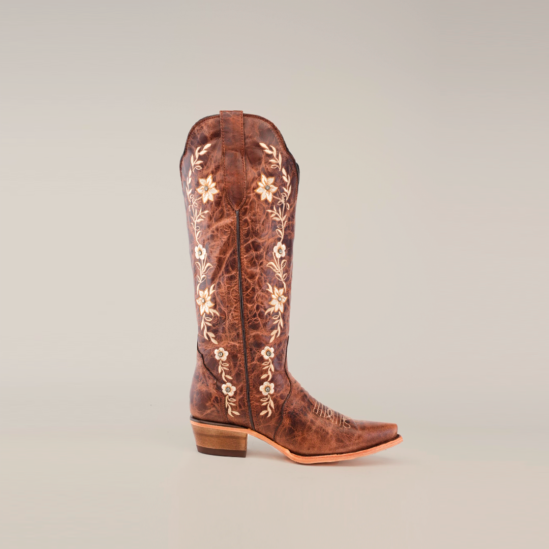 Introducing the handcrafted Mia Brown - Tall Shaft - Snip Toe boot, adorned with exquisite embroidered white floral patterns on premium leather. This elegant piece features a pointed toe and low heel, beautifully presented against a plain white background.