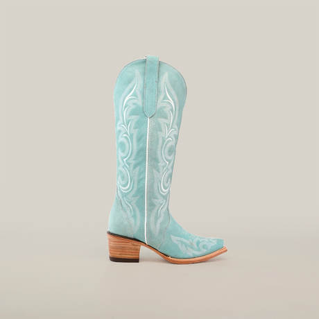 The Amara BB Suede boot is a turquoise cowboy style with a tall shaft and intricate white embroidery. Its crafted from luxurious suede leather and features an elegant snip toe with a wooden heel, set against a plain white background.