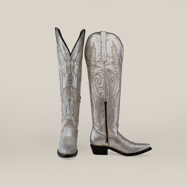 A pair of Brittany Silver Tall Shaft Snip Toe Boots, expertly crafted from premium leather with detailed stitching and side zippers. One boot stands upright while the other leans on a plain backdrop, highlighting their handcrafted elegance.