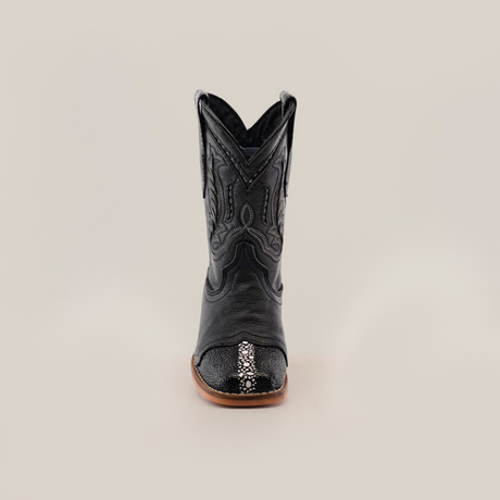 The Stingray Half Cowhide Print Black Rodeo Toe is a black cowboy boot made from cowhide leather with detailed stitching and a textured toe pattern. It features a brown sole and is showcased against a plain white background, exuding classic western charm