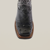 A detailed view of the Karoo Ostrich Half Cowhide Print Black Rodeo Toe boot highlights its western style, showcasing decorative stitching and textured ostrich leather. A brown sole with visible stitching complements the square toe, all set against a plain white backdrop for an elegantly rugged look.