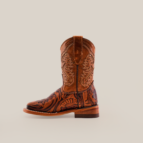 The Handtooled Leave Orix Square Toe is a single brown cowboy boot, adorned with intricate embroidery and floral patterns. Crafted from cowhide leather with a wooden heel, it stands upright on a plain white background, showcasing traditional craftsmanship and classic Western style.