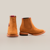 Two Prime Suede Honey Square Toe boots are shown on a white background. The tan leather Chelsea boots have reddish plaid lining, brown soles, and elastic goring; the left boot displays the inner side and the right shows the outer side.