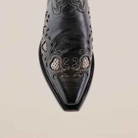 Close-up of the Studded Hearts Black boot, featuring a snip toe and short shaft. Handcrafted with polished black leather, it showcases intricate white embroidery with small heart-like shapes and curving lines, reflecting luxury bootmaking artistry.