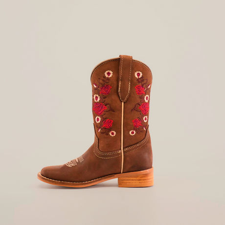 The Mia Copper Suede - Square Toe cowboy boot showcases premium leather craftsmanship with red and white floral embroidery on the shaft, complemented by a wooden heel and a rounded toe against a plain white background.