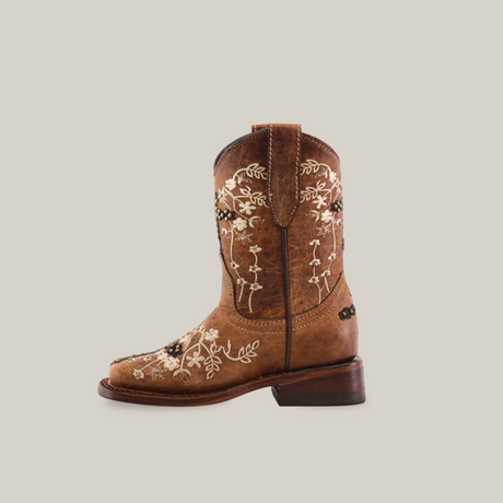 The Margacruz Studs Orix - Square Toe is a mid-calf, low-heel girls cowboy boot crafted from premium brown leather with intricate white floral embroidery against a plain background, adding a touch of Western charm.