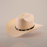 The 5000x Sinaloa Straw Hat, featuring a wide brim and black band adorned with silver oval decorations, exudes elegance and fine craftsmanship as it sits against a plain light background.