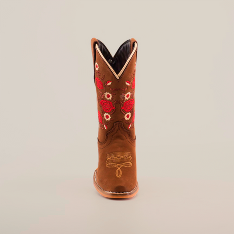 The Mia Copper Suede - Snip Toe boots feature premium leather in a brown cowboy design, complemented by red and white floral embroidery on the shaft. Ankle stitching enhances the look, and a light-colored sole completes the design against a plain white backdrop.