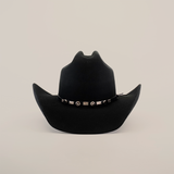 The 6X Leandro Black cowboy hat boasts a wide brim with upward curled sides and a decorative band adorned with shiny conchos and rectangular studs. Crafted from premium sheeps wool, this luxurious hat stands out beautifully against its plain white background.