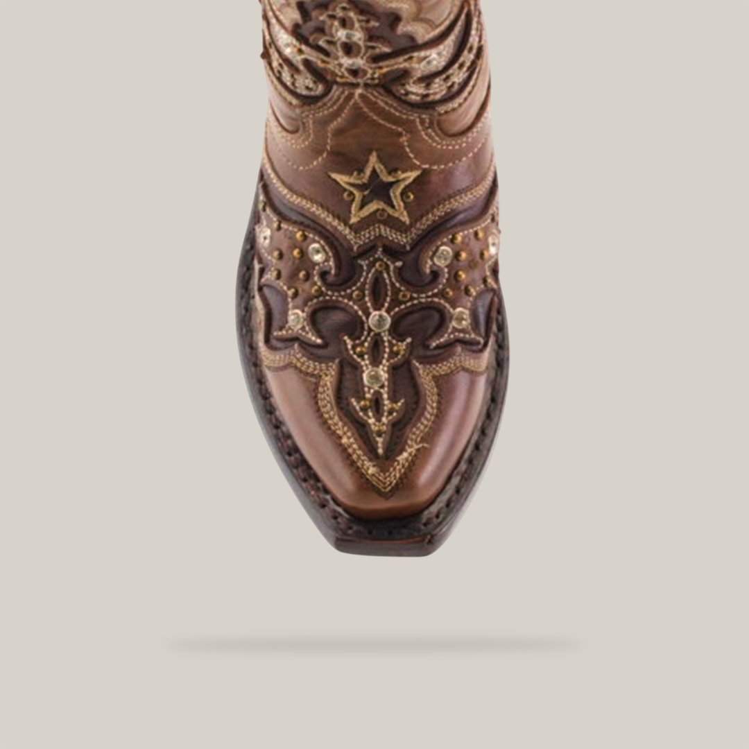 A close-up of the Chantal Crystals Camel - Snip Toe boot showcases ornate embroidery and decorative metal accents on premium cowhide leather. Expert artisanship is evident in the star and swirl patterns. The boot, viewed from above, rests against a plain background.