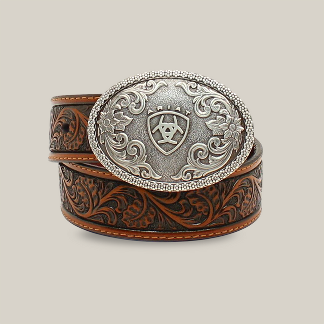 The Ariat Western Boys Belt Youth Leather Floral Embossed Tan - A1300208 features an intricate floral design and a large silver oval buckle with patterns and a central emblem. This coiled belt elegantly merges Western-inspired style with modern flair, part of our youth collection.